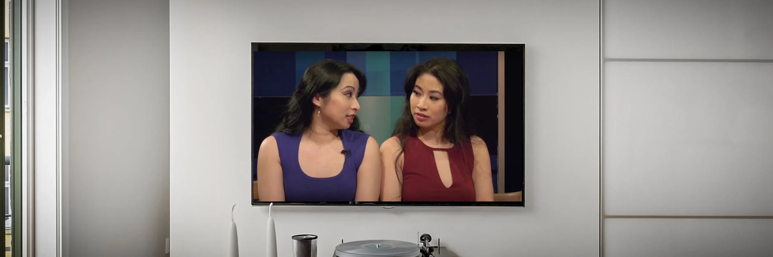 On a living room TV screen, Jacqueline and Stephanie Ko join Access Television to discuss living with myalgic encephalomyelitis (ME/CFS), and Mariposa's 2018 Benefit + Awareness show.