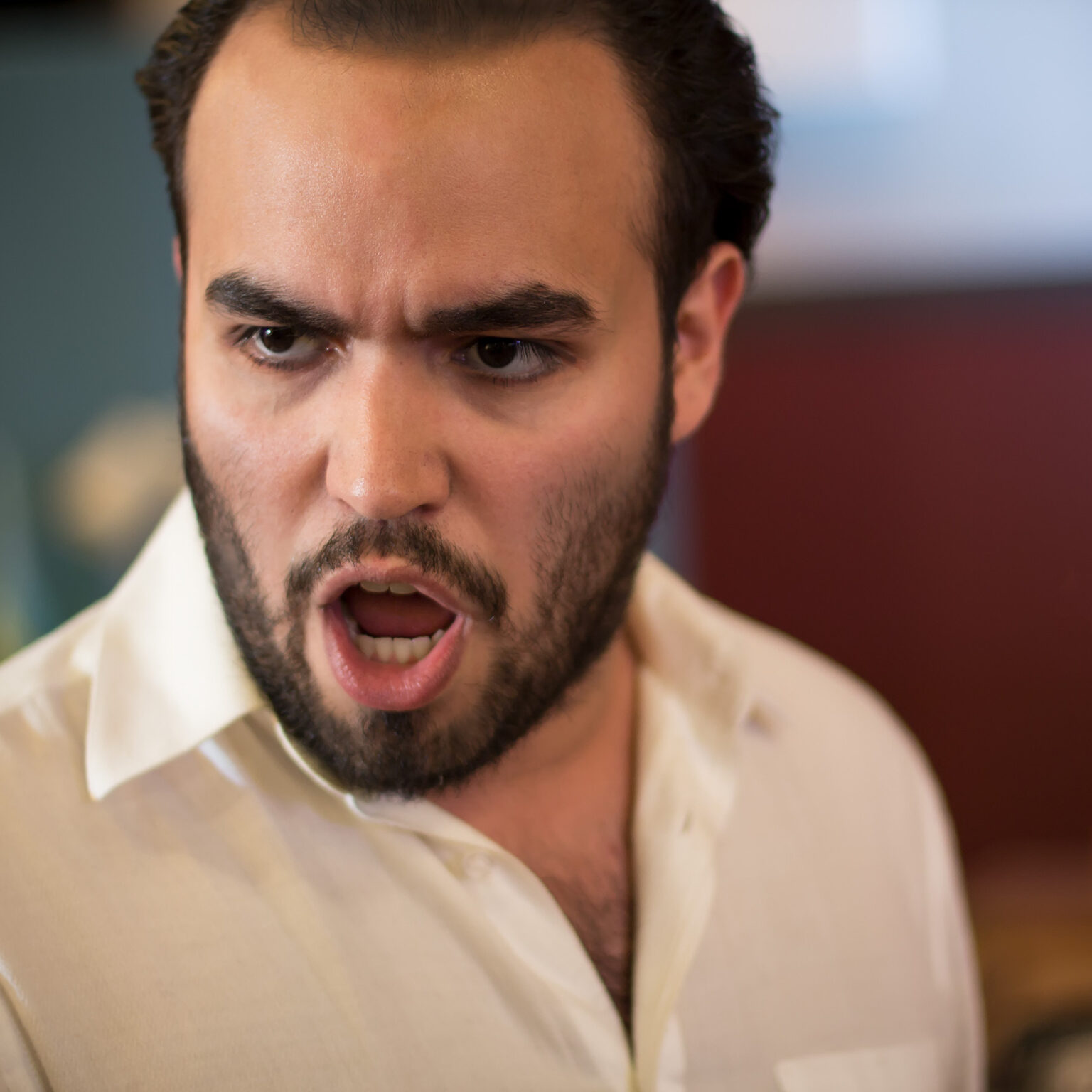 A man of Latino heritage with black hair and a black beard sings onstage with an intense expression on his face.