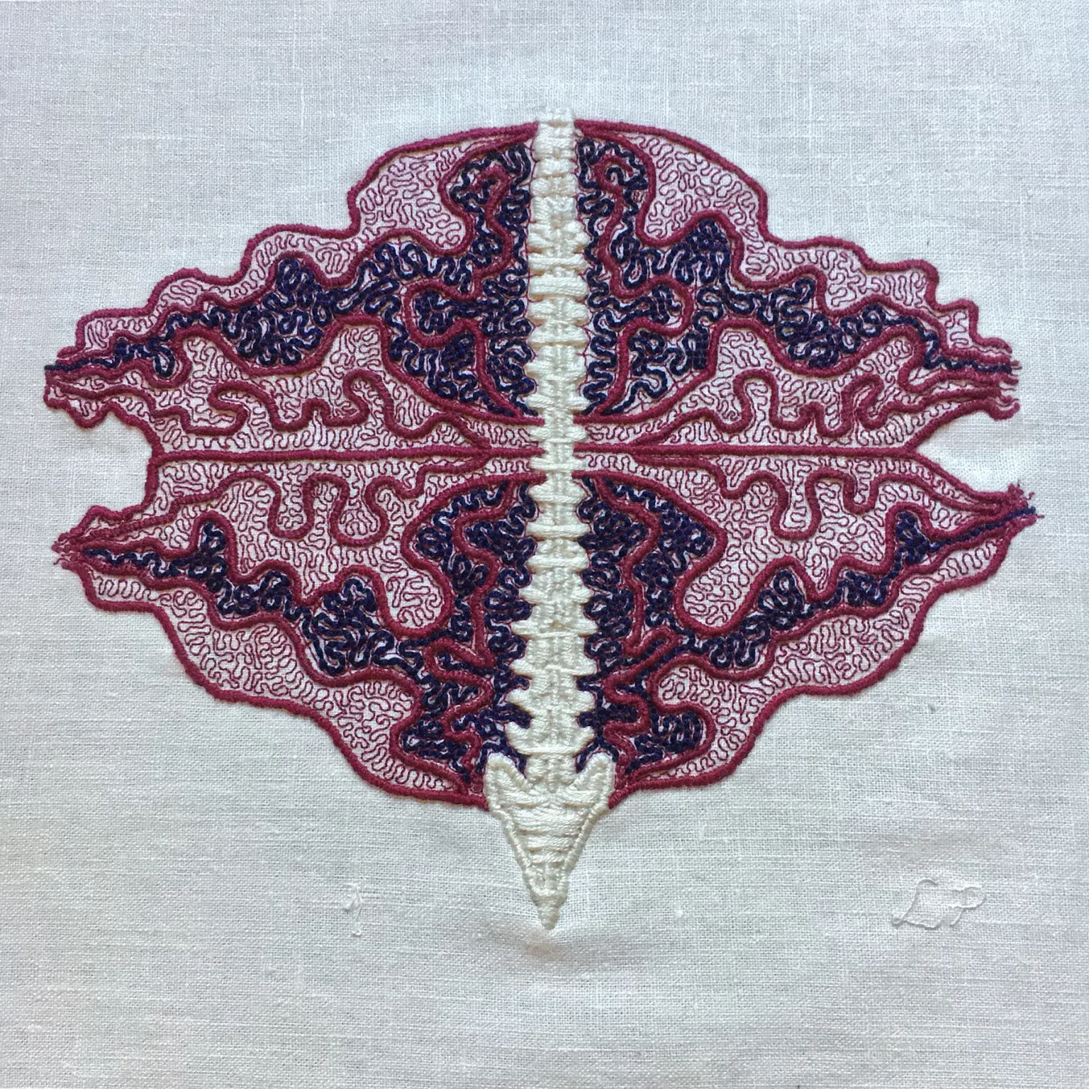 In the centre of some bone white linen, there is a spine embroidered in a thick satin stitch. Emanating from the spine are thick burgundy lines in an undulant oval shape. This oval is bisected across the middle. In the top half, there is a section outlined in burgundy filled with coiling blue lines and a similar section in the bottom half. The rest of the undulant oval is filled with fine coiling burgundy lines. The spine is very straight, the rest of the embroidery is very coiled and busy. Lia’s initials are stitched in fine thread the same colour as the cloth at the bottom right.