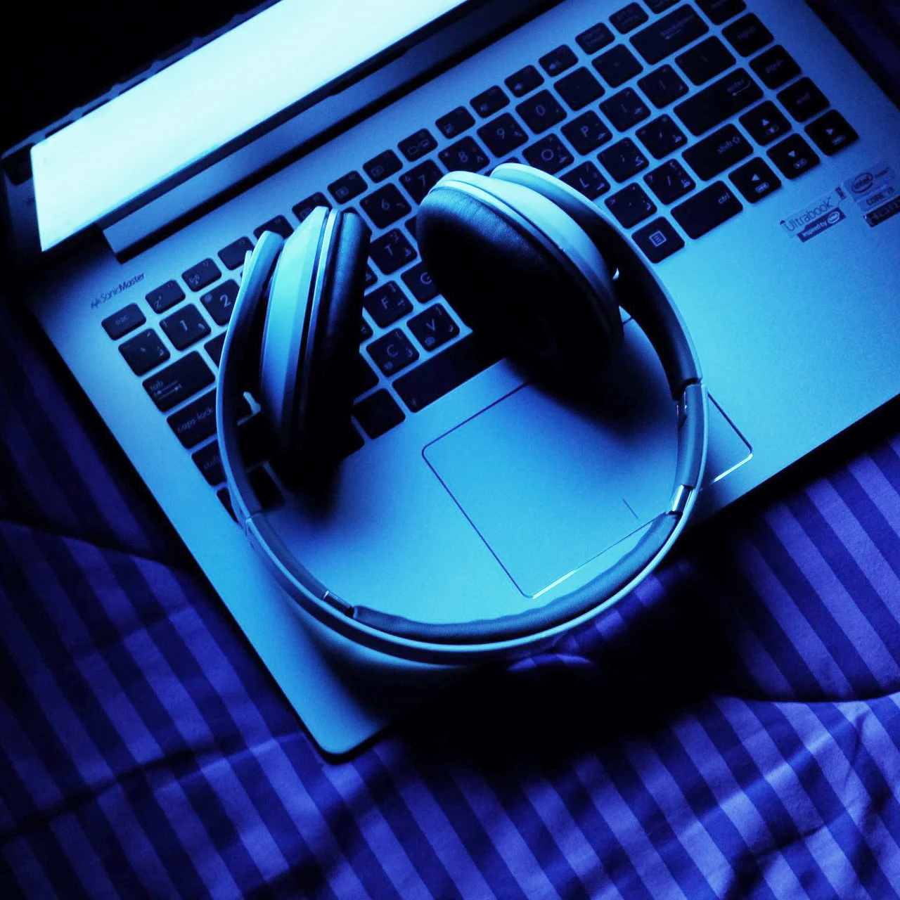 Blue-tinted overhead view of headphones on top of a laptop keyboard