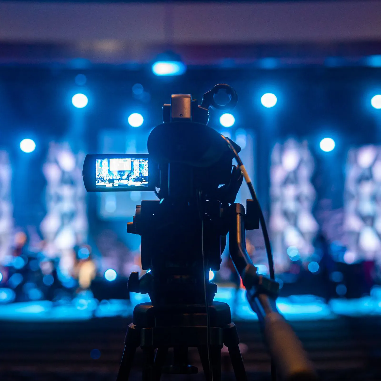 A video camera films a stage lit in blue light