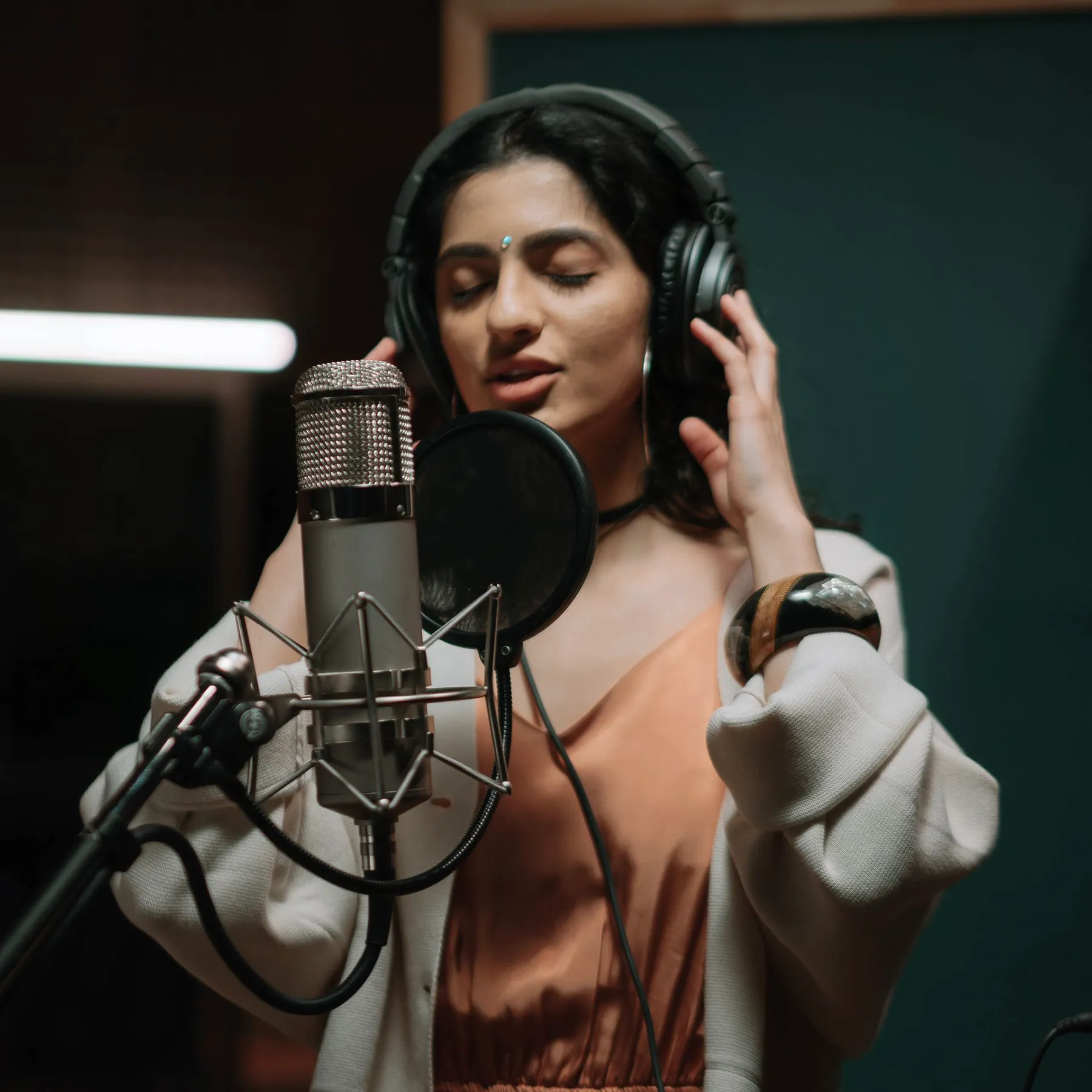 South Asian woman recording with headphones and a studio microphone